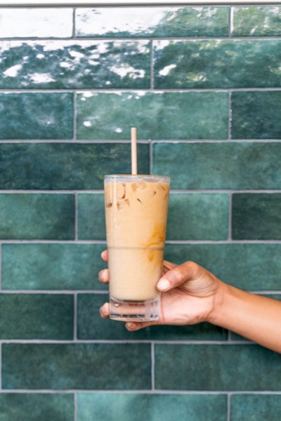An iced coffee held up against the green tiled wall at Toscas